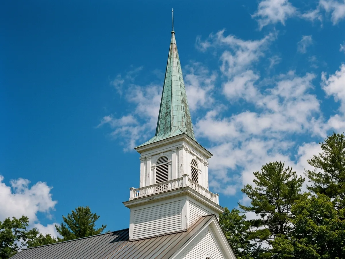 Copper-clad church steeple with a weathered green patina rising above a standing seam roof