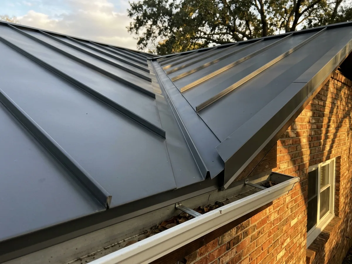 Close-up of painted Galvalume standing seam panels in charcoal on a brick ranch